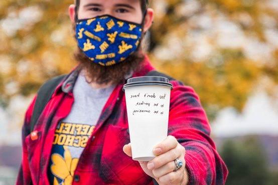 Student holds a cup of coffee with a positive message on it on the Quad at WVU Potomac State College